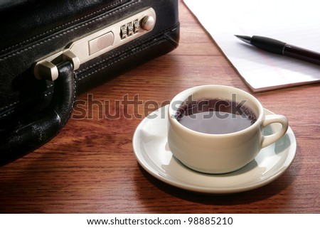 Steamy hot cup of black coffee with warm steam and pen on paper notepad with businessman briefcase on an office conference table desk during a business meeting break at work