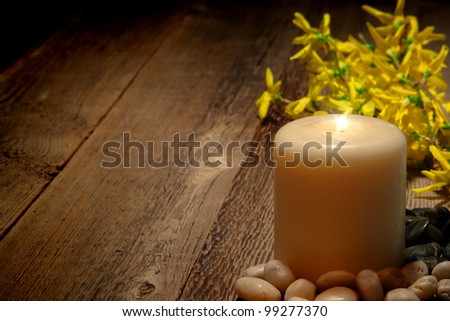 Spiritual meditation and reflection pillar candle burning with bright sparkling flame and blooming yellow forsythia flowers on old weathered wood planks for commemorative remembrance ceremony memorial