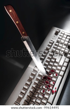 Bloody cyber crime attack scene with a knife as a violent stabbing weapon planted into a computer keyboard with splattered blood as metaphor for online criminal activity and Internet violence danger