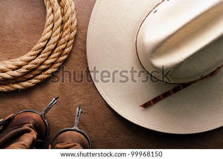 American West rodeo cowboy traditional white straw hat with roping lasso rope and vintage western riding spurs on brown leather boots over hide background