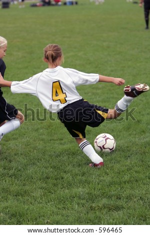 Girl giving it her all during a soccer game.  She is just getting ready to kick the ball as her opponent moves in.