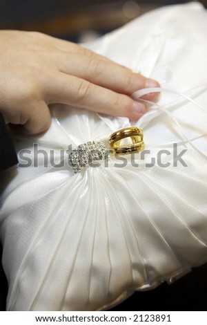 Wedding rings and wedding bands tied onto the ring bearers pillow.  The wedding bands are gold and the wedding ring contains many diamonds.  Focus is on the rings.