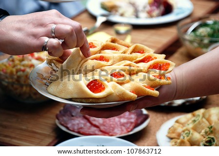 woman takes a pancake with red caviar
