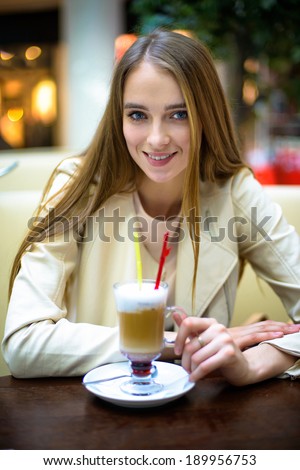 Beautiful smiling woman drinking coffee coctail in cafe