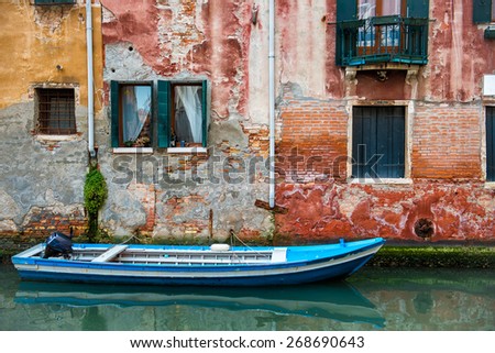 Venice cityscape, boat on narrow water canal near colorful wall with windows