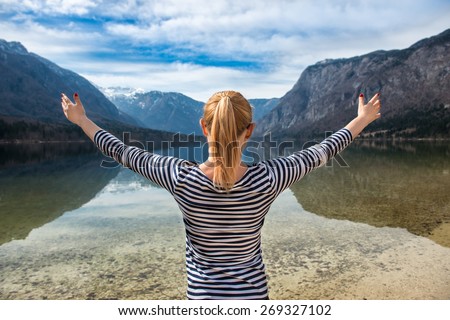 young freedom woman hold hands up near mountain lake