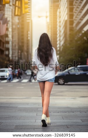 Beautiful woman with long legs walking around New York City street wearing jeans shorts. Rear view.