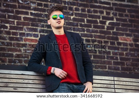 Handsome fashion man wearing casual jacket and sunglasses  standing near brick wall