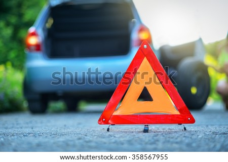 Changing the tire on a broken down car on a road with red warning triangle