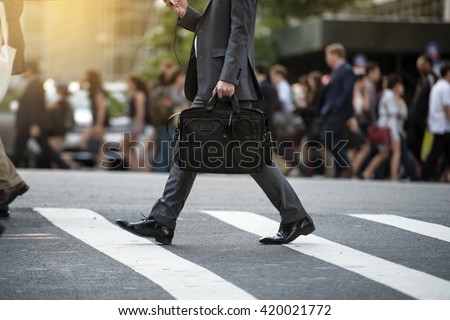 Businessman crossing the street on crosswalk and holding a laptop bag and smatphone in the city