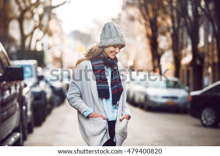 Happy young adult woman walking at beautiful autumn city street wearing colorful scarf and warm hat.