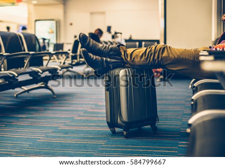 Passenger with carry on luggage waiting for the delay flight in the airport terminal and relaxing.