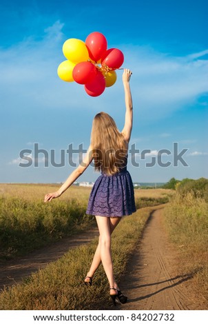 girl in short dress walking along a country road with the balloons in his hands