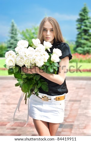 beautiful young girl goes to the park with a large bouquet of white roses