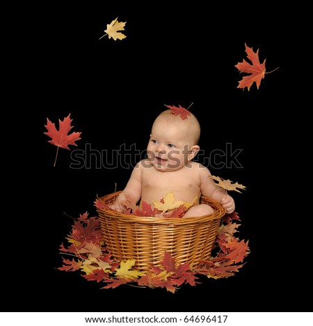 Adorable baby girl sitting in a basket with fall leaves, isolated on a black background.