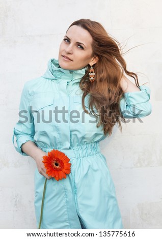 The beautiful girl with a long fair hair in a white blouse and with a flower in her hands
