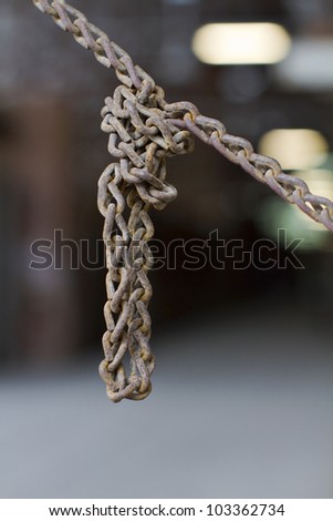 Old rusted steel chain tied in a knot with a short loop hanging down. Closeup view, blur background, vertical, copy space.