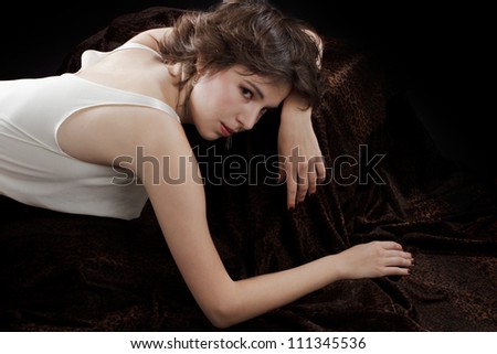 Beautiful young dark haired woman in sexy silk sleeveless blouse. She is gracefully prone on dark leopard velvet fabric. Closeup, dark background, copy space.