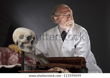 Evil doctor with surgical tools and bloody corpse. Sinister expression, dark background with dramatic low angle spot lighting. Horizontal, copy space.