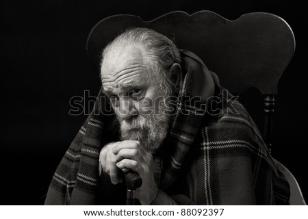 Serious sad old man in his seventies seated with a plaid shawl over his shoulders