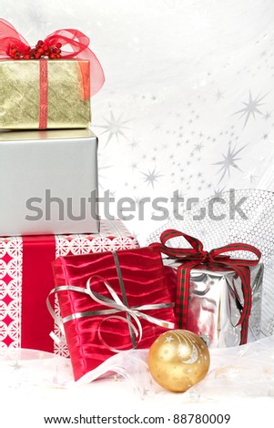 Still life with red, silver, gold wrapped Christmas gifts, pretty ribbons and ornaments. Silver star translucent fabric backdrop on white. Vertical format with copy space.
