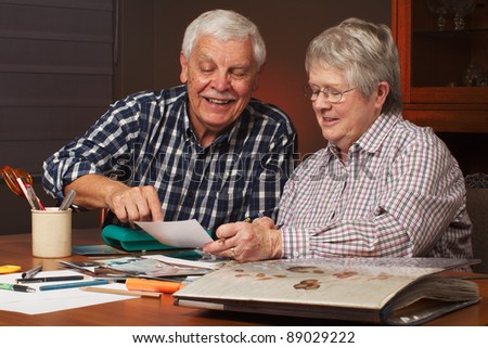Happy senior married couple sharing memories while  working on family photo  album together. Horizontal format.