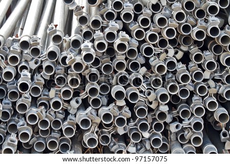 Large stack of steel pipes used for chain link fence posts, showing abstract circular pattern of open ends. Horizontal layout.