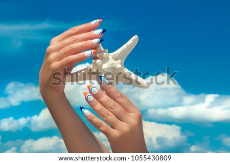 Marine nail design.Long French manicure with orange and blue nail Polish on female hand close up sea star on the sky of the sea.