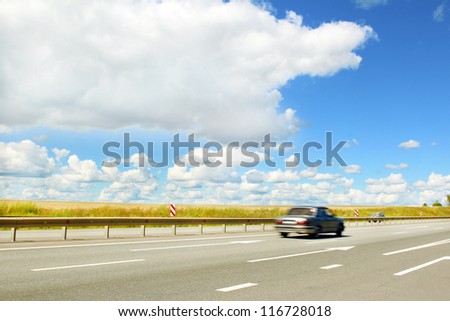 The car moves along an asphalt road in cloudy weather in the summer.