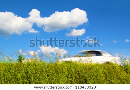 White car coming up the road on the background of the sky with clouds and green grass in the warm summer season.