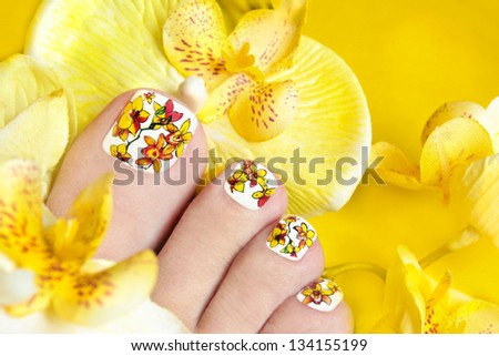 Pedicure with orchids in the women\'s legs on a yellow background.