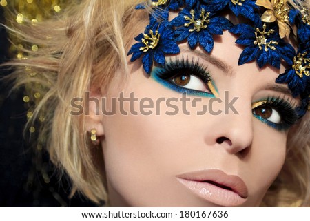 Luxurious blue makeup on a girl with blond hair and decorative flowers on her head.