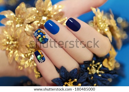 Nails of women covered in blue lacquer different shades with rhinestones and with flowers in his hand.