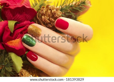 Multicolor manicure with red,green and yellow brilliant varnish for the nails on a yellow background with rose and Christmas tree.