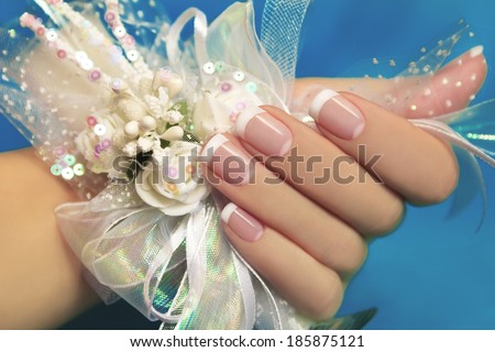 Wedding manicure on female hand with festive decoration of white ribbons and flowers