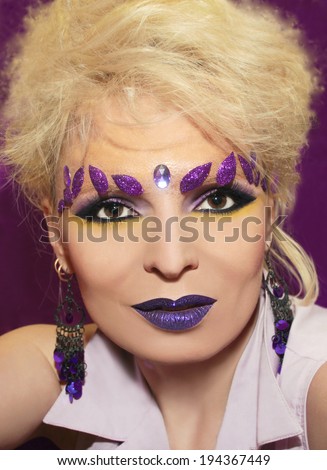Purple makeup with glistening lips and leaves on the brow of a girl with blond hair