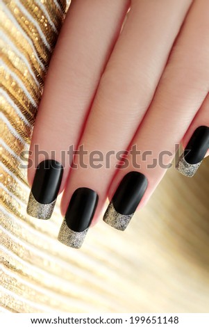 Black French manicure with Golden shining varnish on striped background