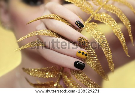 Caviar manicure in yellow black nails with black and gold rhinestones with brilliant ornament in his hand.