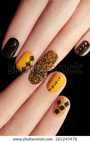 Caviar manicure in yellow black nails with black and gold rhinestones on a black background.