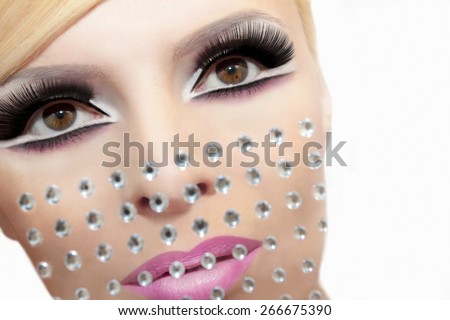 Makeup with rhinestones on the girl\'s face with black eyelashes and a pink lipstick.