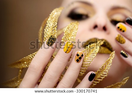 Yellow black manicure with metallic crystals of different shapes and colors on short nails.