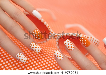 Sunny orange manicure with dots on the women\'s nails closeup.