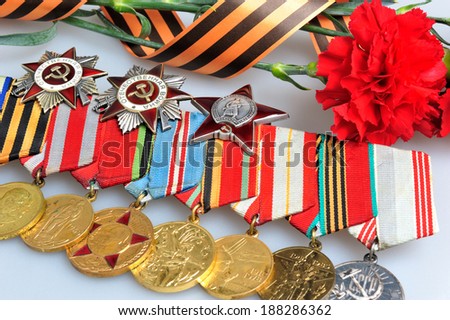 Red carnations tied with Saint George ribbon and medals with orders on gray background closeup