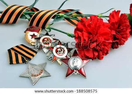 Red carnations tied with Saint George ribbon and five orders of Great patriotic war on gray