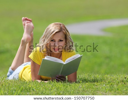 Girl reading the book. Blonde beautiful young woman with book lying on the grass. Outdoor. Sunny day. Back to school. Looking at the camera