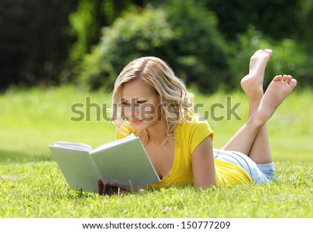 Girl reading the book. Blonde beautiful young woman with book lying on the grass. Outdoor. Sunny day. Back to school