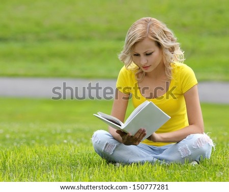 Girl reading the book. Blonde beautiful young woman with book sitting on the grass. Outdoor. Sunny day. Back to school