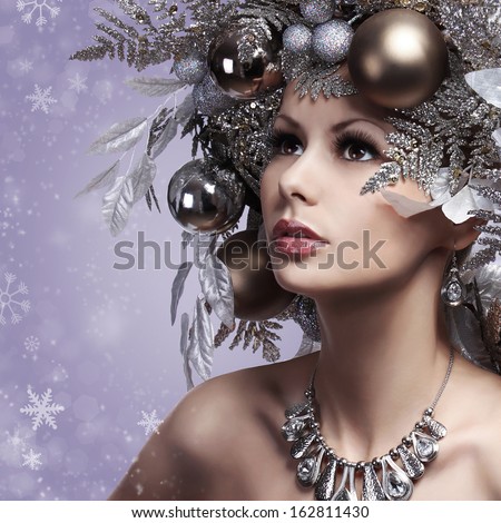 Christmas Woman with New Year Decorated Hairstyle. Snow Queen. Portrait of Fashion Girl with Silver and Gold Christmas Balls over Snowflakes background. Holiday Card