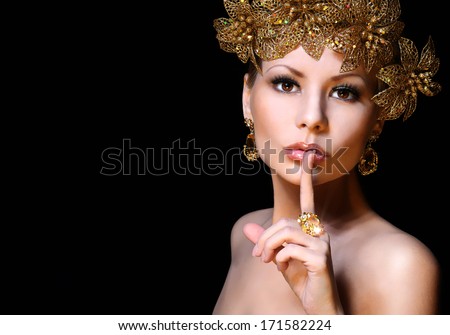 Fashion Girl With Gold Jewelries Over Black Background. Beauty Young Woman With Finger On Her Sexy Lips Showing Hush. Decorated Hairstyle. Luxury Portrait