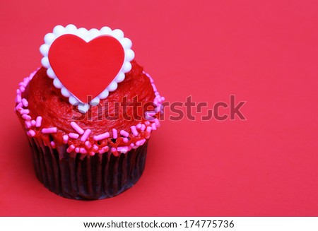 Chocolate cupcake with red heart on the top, over red background with space for the text.